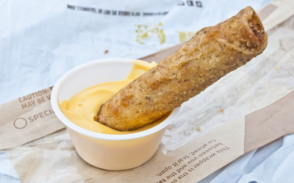 A taquito being dipped in cheese