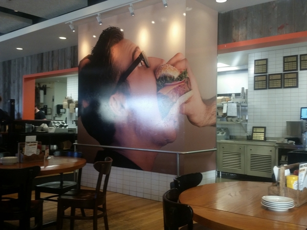 A gigantic mural of a man getting a hamburger forcibly shoved into his mouth.