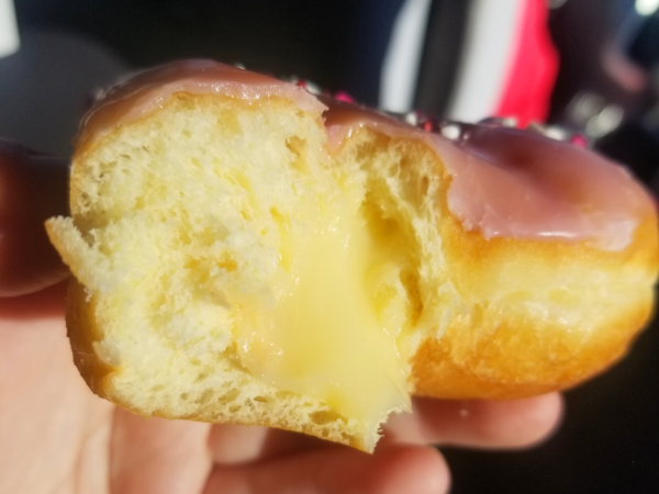 A partially-eaten donut with pink frosting and cream filling.